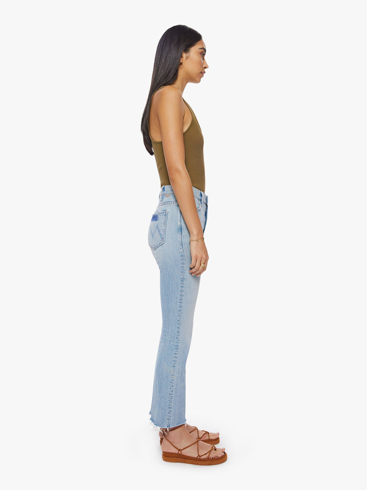 Side view of a woman light blue high-rise flare has an ankle-length inseam and a raw hem.