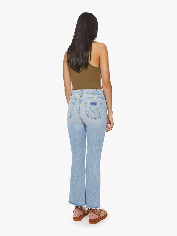 Back view of a woman light blue high-rise flare has an ankle-length inseam and a raw hem.