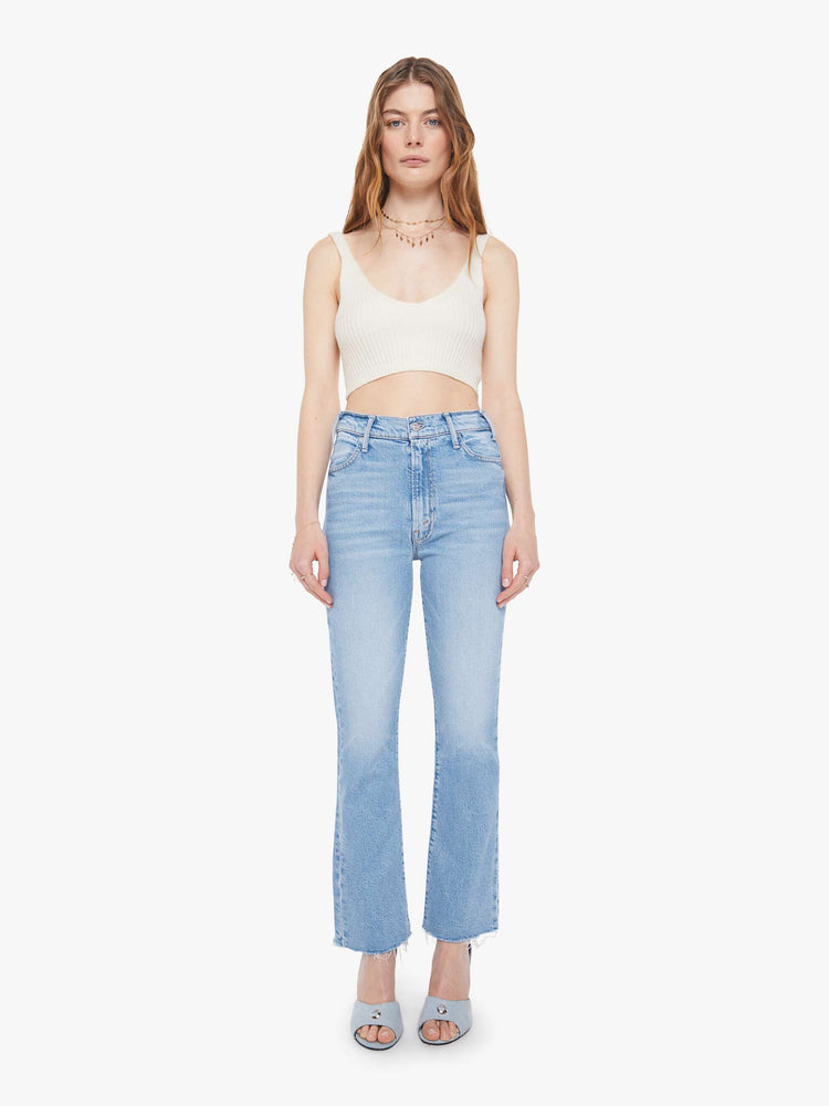 Front view of a woman in a light blue high-rise flare jeans have an ankle-length inseam, zip fly and a raw hem.