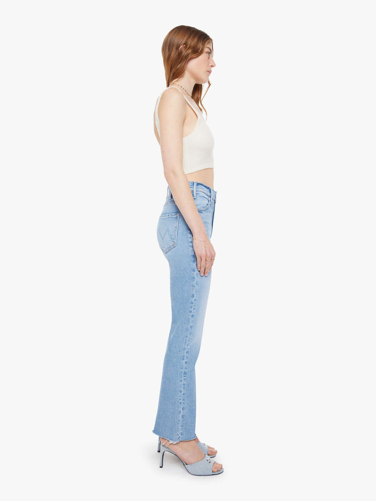 Side view of a woman in a light blue high-rise flare jeans have an ankle-length inseam, zip fly and a raw hem.