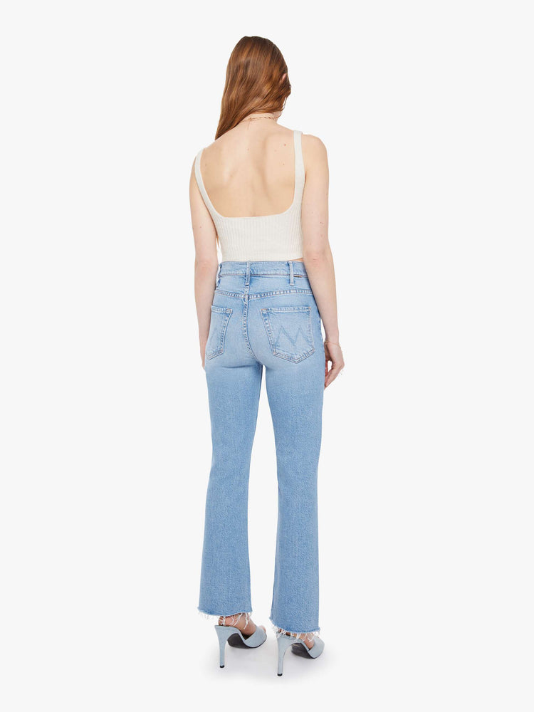 Back view of a woman in a light blue high-rise flare jeans have an ankle-length inseam, zip fly and a raw hem.