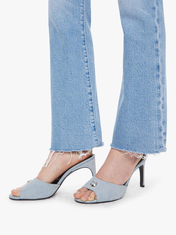 Hem view of a woman in a light blue high-rise flare jeans have an ankle-length inseam, zip fly and a raw hem.