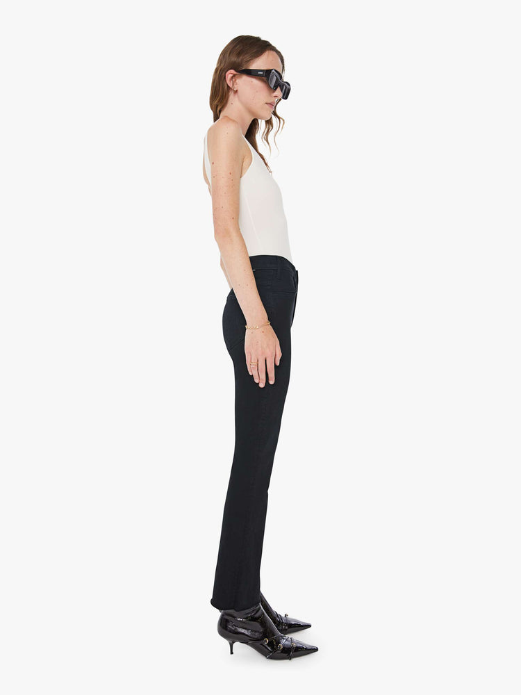 Side view of a womens black jean featuring a high rise, a flare leg, and an ankle length raw hem.