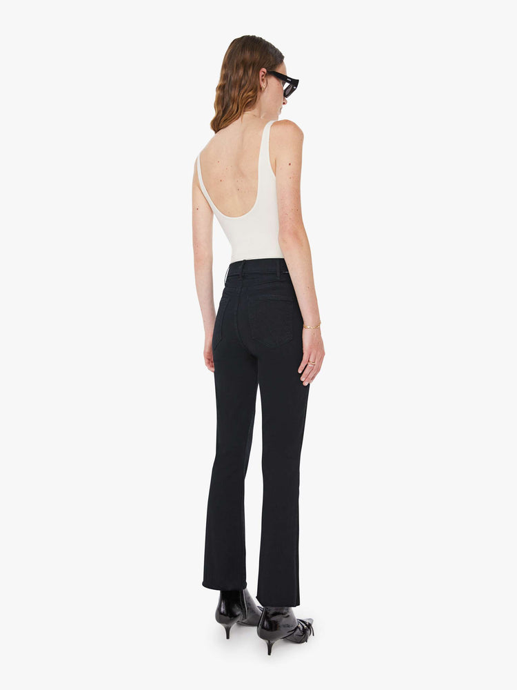 Back view of a womens black jean featuring a high rise, a flare leg, and an ankle length raw hem.