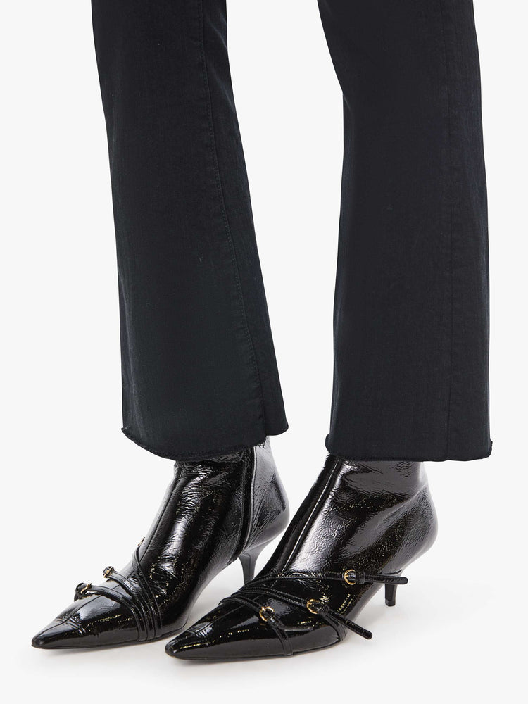 Hem view of a womens black jean featuring a high rise, a flare leg, and an ankle length raw hem.