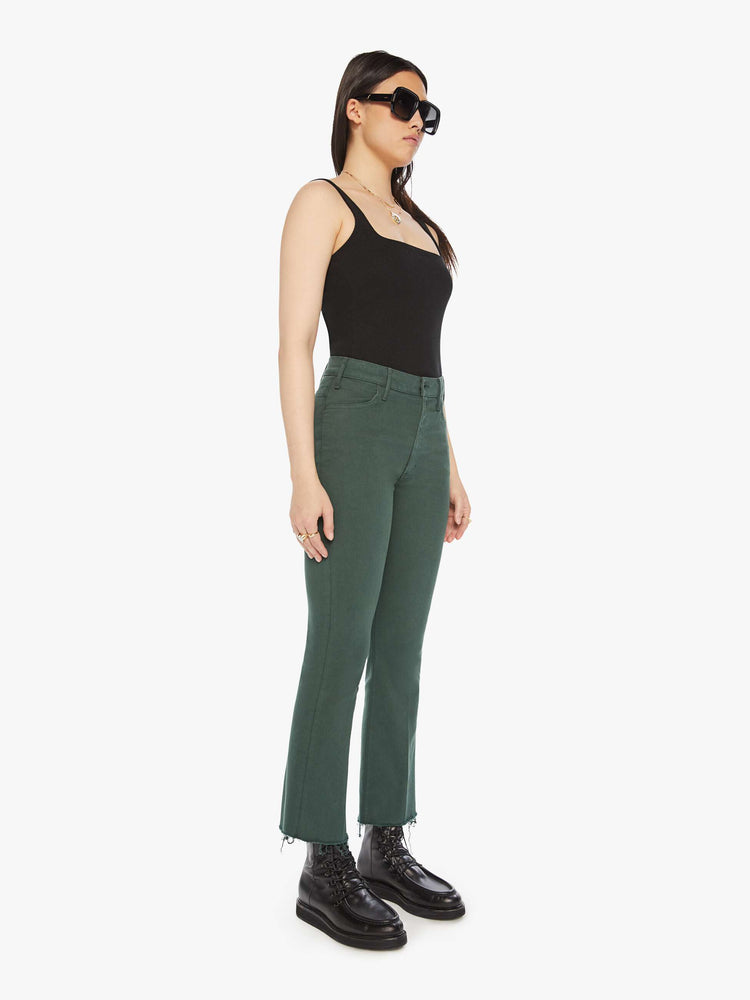 Side angle view of a woman high-rise flare has an ankle-length inseam and a raw hem in a forest green.