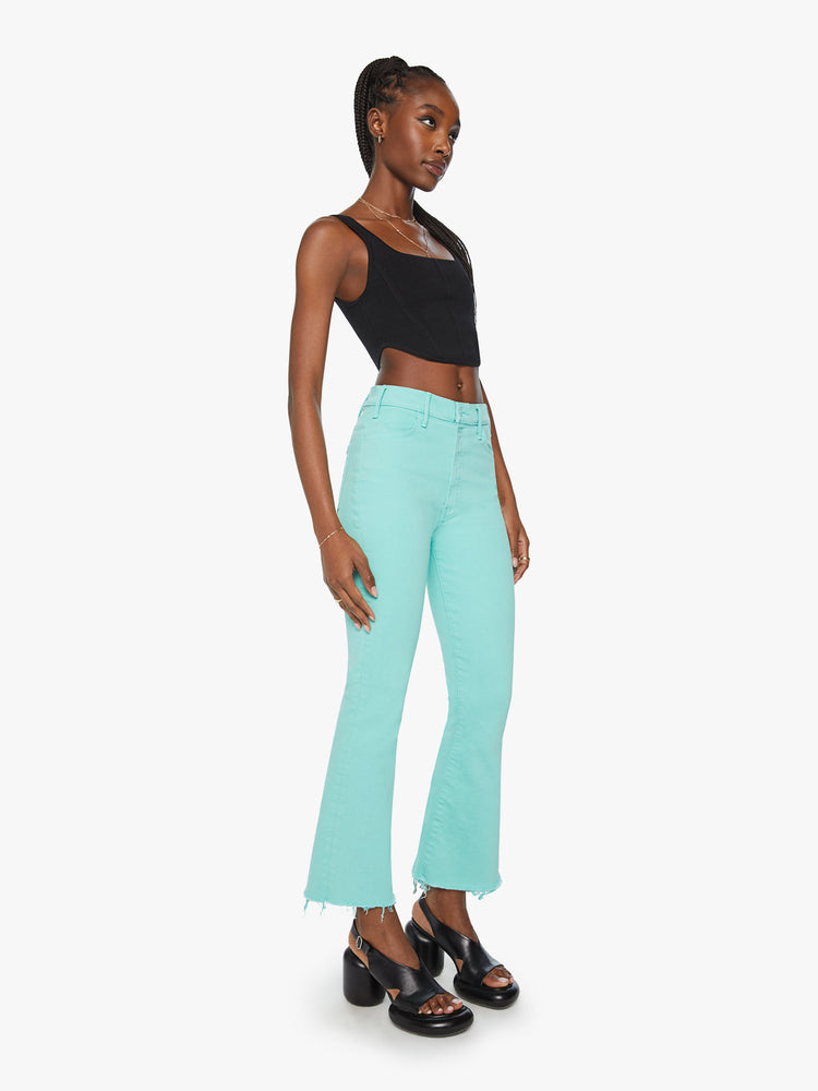 Side angle view of a woman high-rise flare has an ankle-length inseam and a raw hem in a light blue aqua blue.