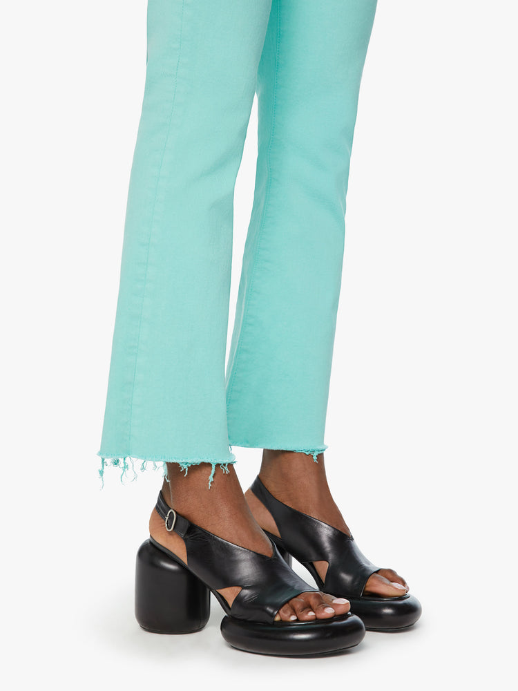 Hem view of a woman high-rise flare has an ankle-length inseam and a raw hem in a light blue aqua blue.
