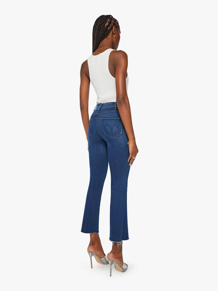 Back view of a womens dark blue wash jean featuring a high rise and an ankle length flare with raw hem.