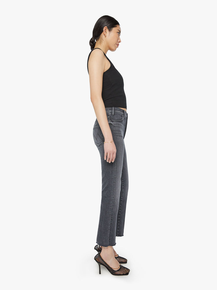 Side view of woman high-rise flare has an ankle-length inseam and a raw hem in a faded black.