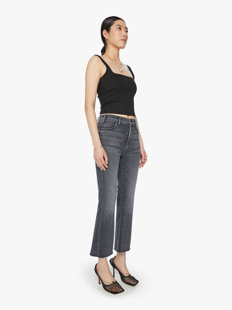 Side angle view of woman high-rise flare has an ankle-length inseam and a raw hem in a faded black.