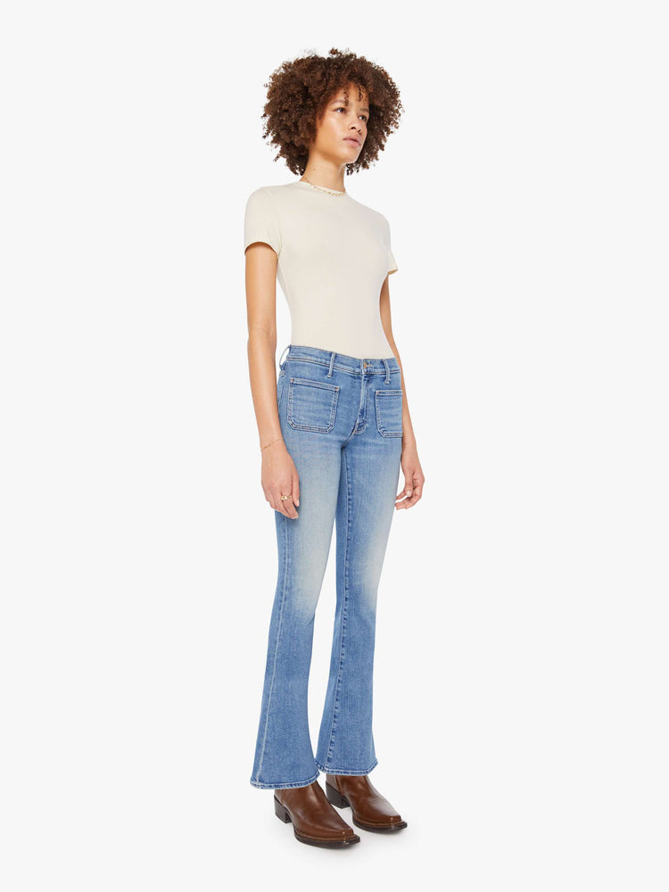 Side angle view of a woman in  a mid rise flare, zip fly, patch pockets, a 31-inch inseam and a clean hem.