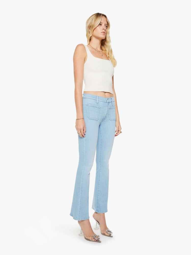 Front angled view of a woman in a light blue  flare has a mid rise, zip fly, patch pockets, a 31-inch inseam and a clean hem. 