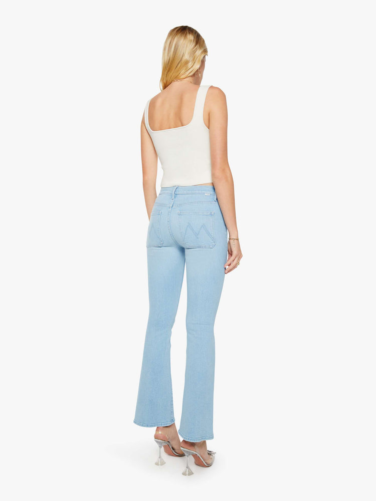 Back view of a woman in a light blue  flare has a mid rise, zip fly, patch pockets, a 31-inch inseam and a clean hem. 