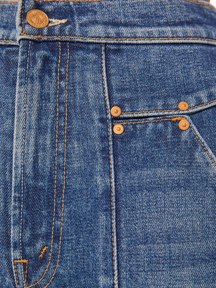 Swatch view of a woman in a mid-blue high-waisted jeans with a wide straight leg, zip fly, patch pockets with rivet details, a seam down the front and back and a clean 32-inch inseam.