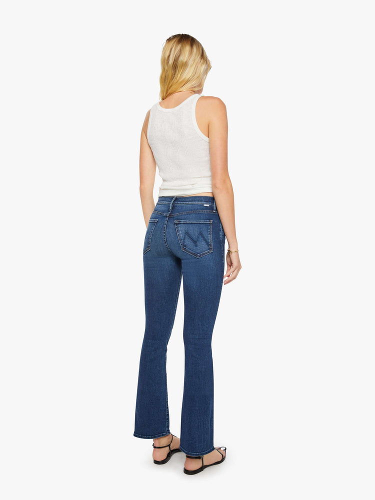 Back view of a woman in a dark blue high-waisted bootcut jeans with a zip fly and a 31-inch inseam with a clean hem.