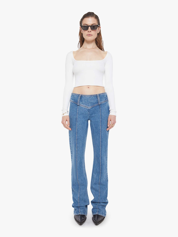 Front view of a woman in a mid blue  low-rise jeans feature an extra-wide waistband with a side-zip closure, a slightly flared leg with pintuck details down the front and a long 34-inch inseam with a clean hem. 