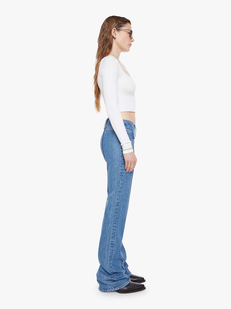 Side view of a woman in a mid blue  low-rise jeans feature an extra-wide waistband with a side-zip closure, a slightly flared leg with pintuck details down the front and a long 34-inch inseam with a clean hem. 
