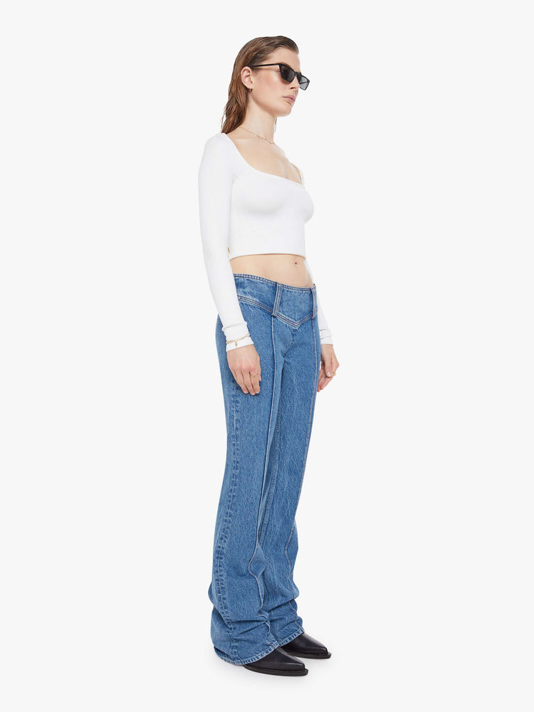 Front view of a woman in a mid blue  low-rise jeans feature an extra-wide waistband with a side-zip closure, a slightly flared leg with pintuck details down the front and a long 34-inch inseam with a clean hem. 