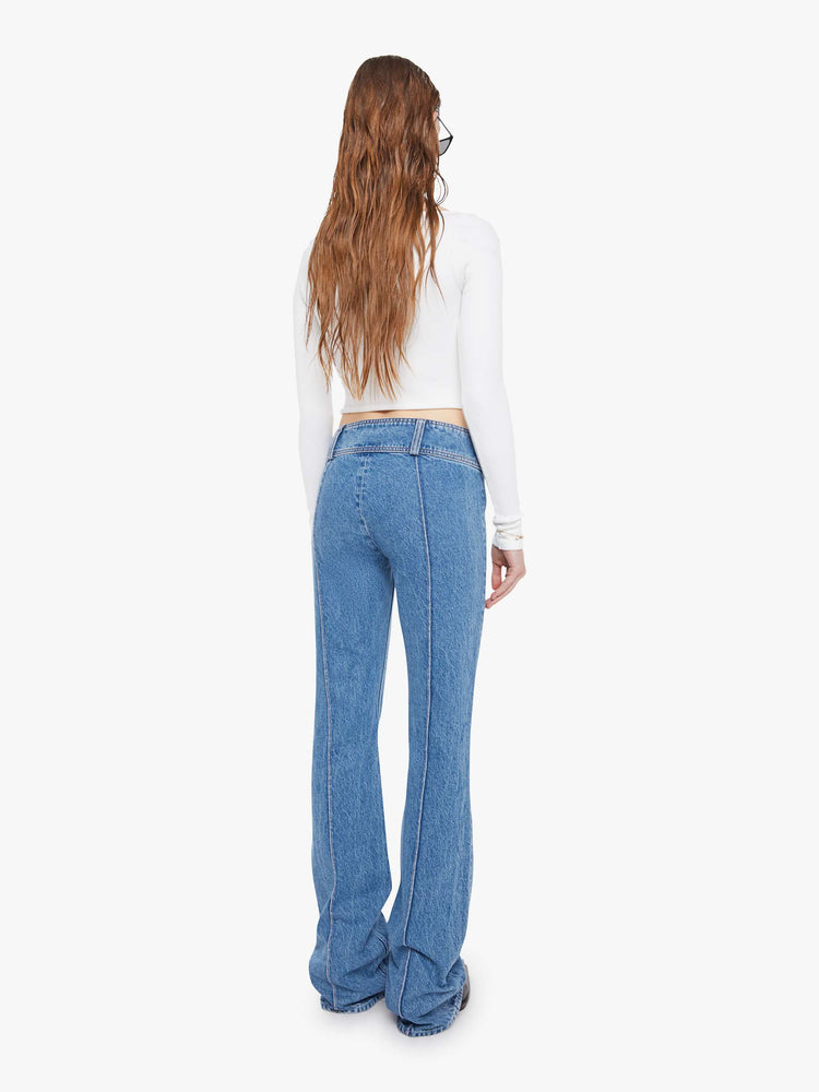 Back view of a woman in a mid blue  low-rise jeans feature an extra-wide waistband with a side-zip closure, a slightly flared leg with pintuck details down the front and a long 34-inch inseam with a clean hem. 