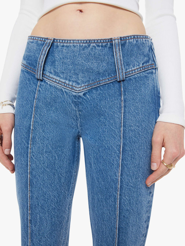 Close up view of a woman in a mid blue  low-rise jeans feature an extra-wide waistband with a side-zip closure, a slightly flared leg with pintuck details down the front and a long 34-inch inseam with a clean hem. 