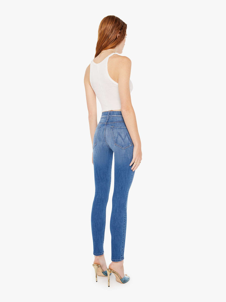 Back view of a woman wearing a medium blue wash jean featuring a high rise and a skinny leg, paired with a white tank top.