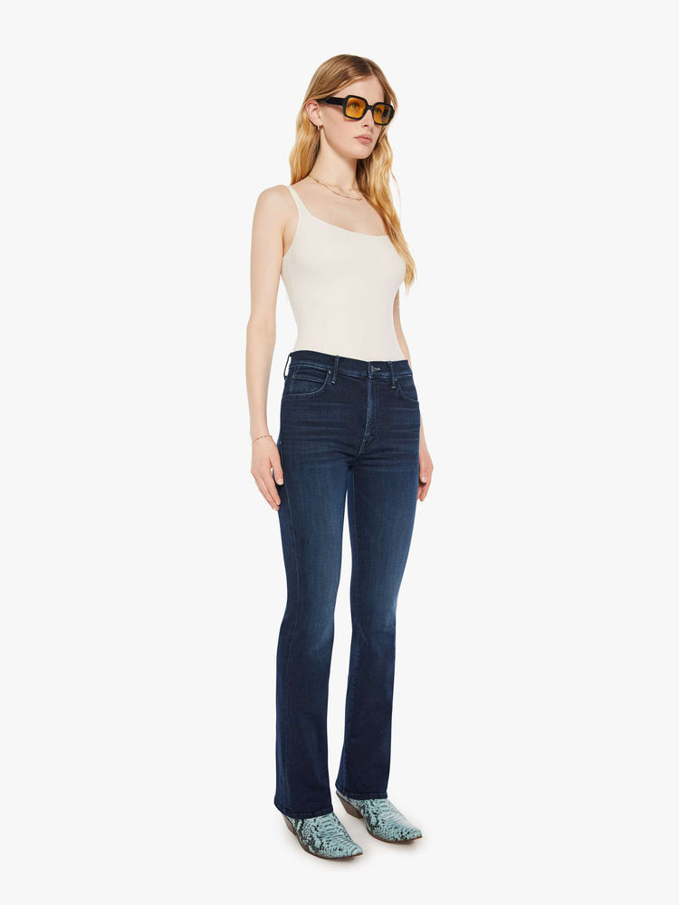 Side angle view of a woman in a dark blue mid-rise jeans with a flared leg, zip fly and a long 31-inch inseam with a clean hem. 