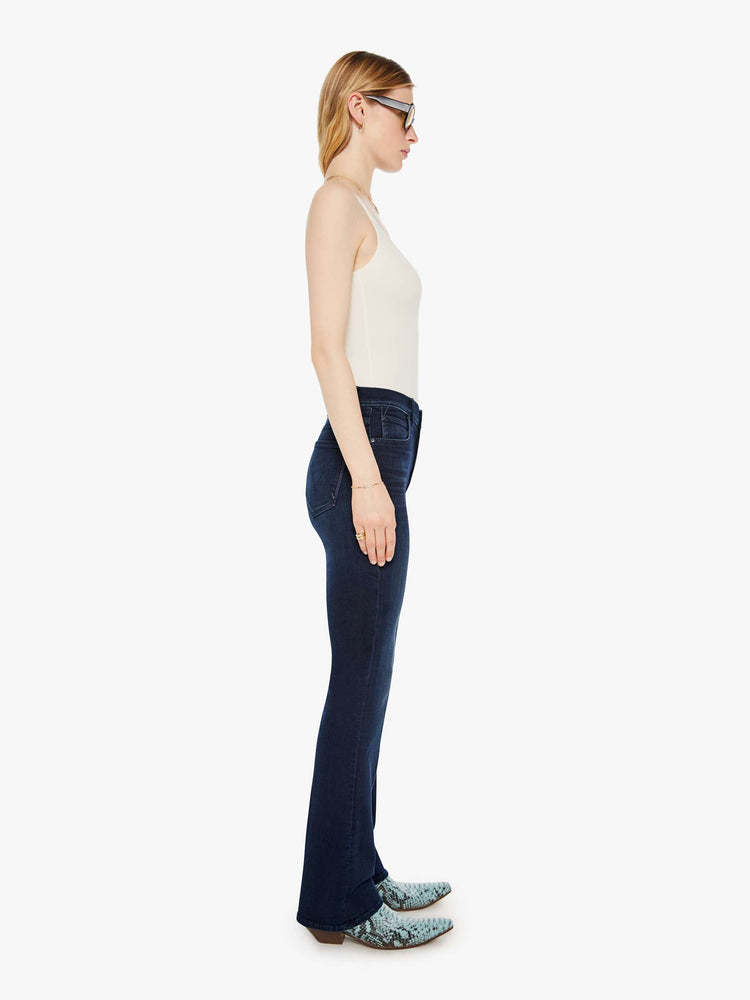 Side angle view of a woman in a dark blue mid-rise jeans with a flared leg, zip fly and a long 31-inch inseam with a clean hem. 