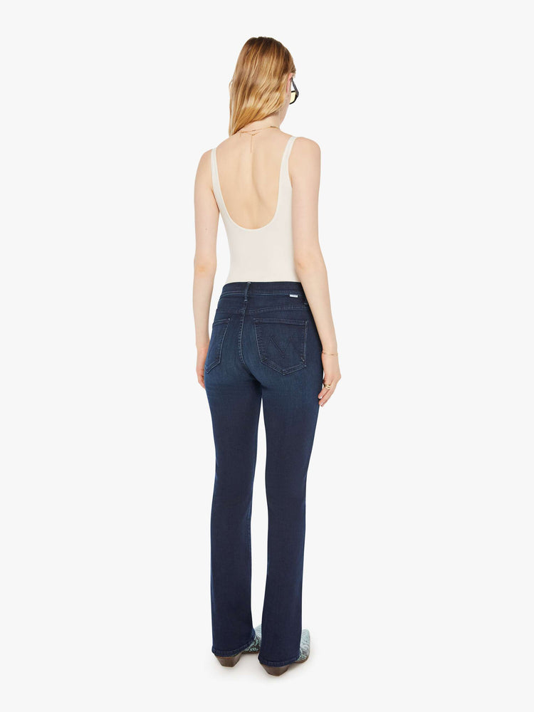 Back view of a woman in a dark blue mid-rise jeans with a flared leg, zip fly and a long 31-inch inseam with a clean hem. 