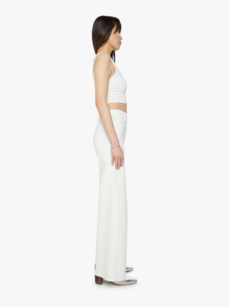 Side view of a woman white wide leg pants with a high rise, long 32-inch inseam and a frayed hem.