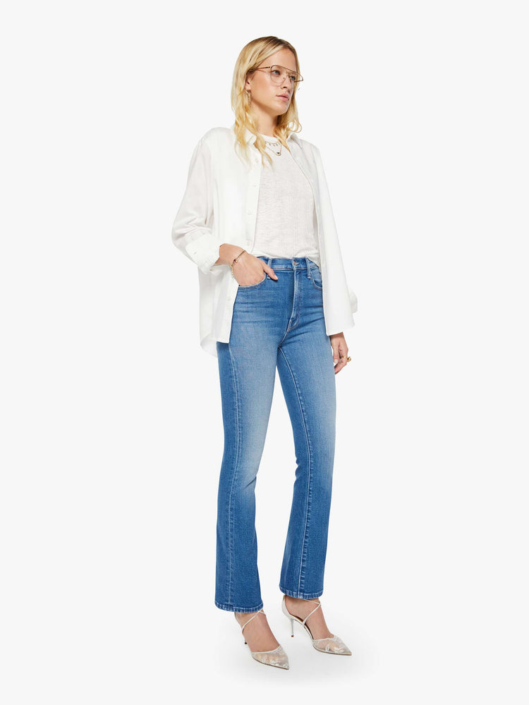 Side angle view of woman in a mid blue high-rise flare has a zip fly, 31-inch inseam and a clean hem.