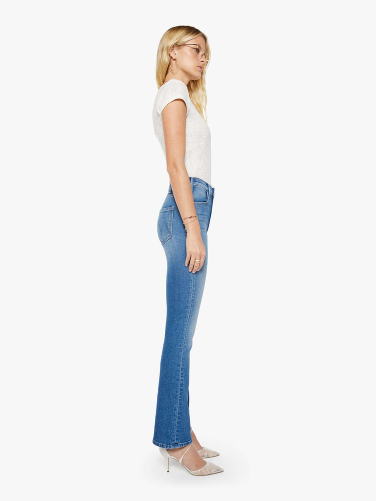 Side view of woman in a mid blue high-rise flare has a zip fly, 31-inch inseam and a clean hem.