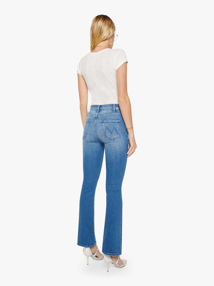 Back view of woman in a mid blue high-rise flare has a zip fly, 31-inch inseam and a clean hem.