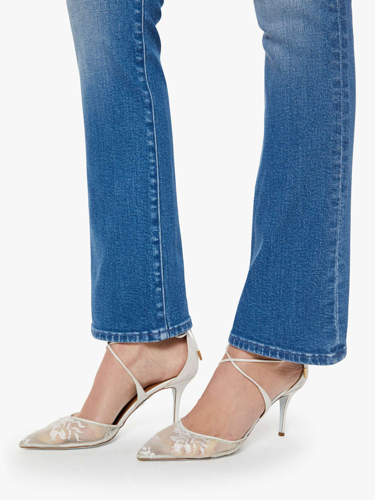 Hem view of woman in a mid blue high-rise flare has a zip fly, 31-inch inseam and a clean hem.
