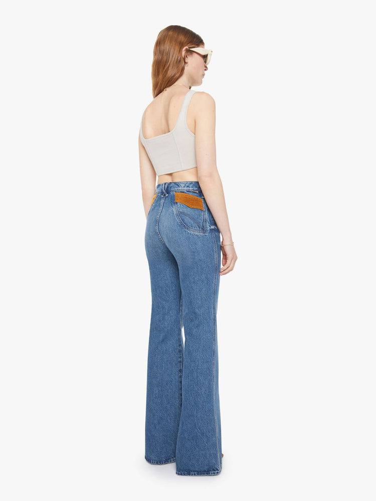 Back view of a woman in a mid blue high-rise flare with a zip fly, off-center back pockets, a long 34-inch inseam and a clean hem.