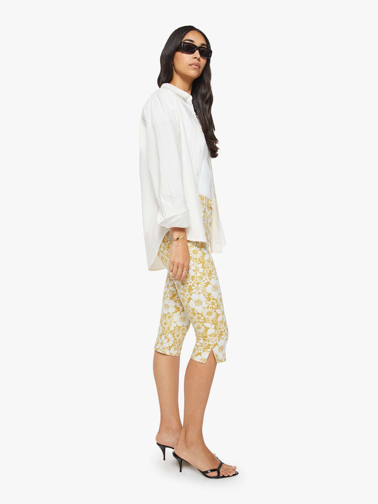 Side view of a woman in a off white with golden yellow floral print high-waisted pants with a skinny leg, zip fly and a capri-length inseam.