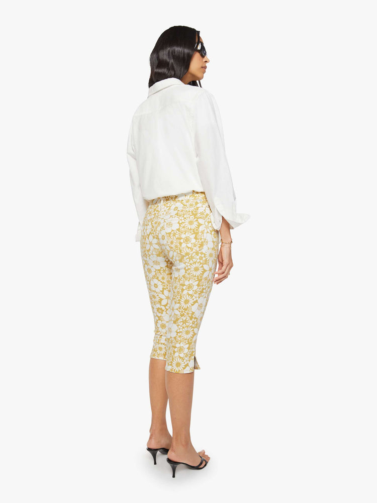 Back view of a woman in a off white with golden yellow floral print high-waisted pants with a skinny leg, zip fly and a capri-length inseam.