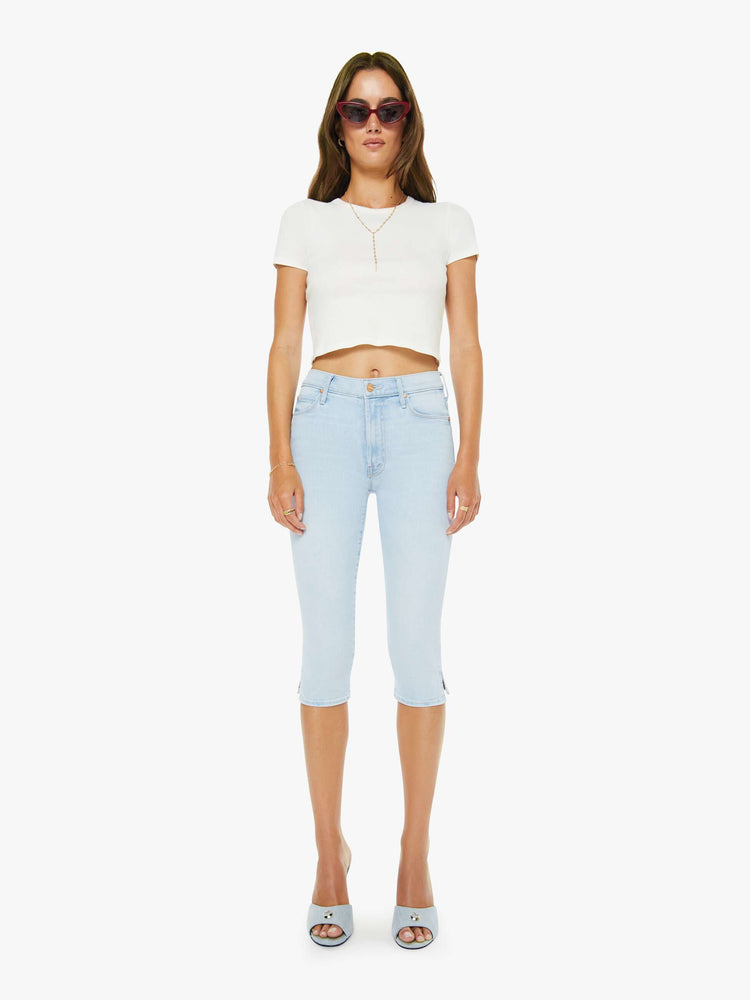 Front view of a woman in a light blue high-waisted pants with a skinny leg, zip fly and a capri-length inseam.