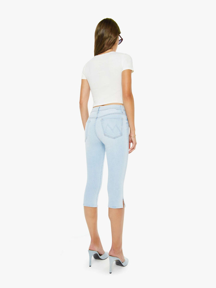 Back view of a woman in a light blue high-waisted pants with a skinny leg, zip fly and a capri-length inseam.