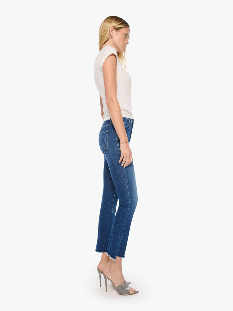 Side view of a woman in a md blue high-waisted bootcut is cropped at the ankle with a frayed step-hem.