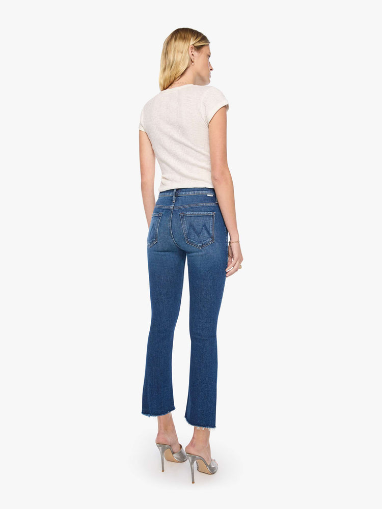 Back view of a woman in a md blue high-waisted bootcut is cropped at the ankle with a frayed step-hem.