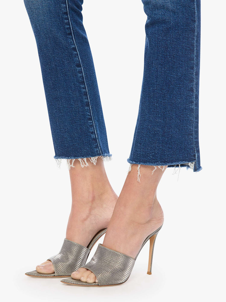Hem close up view of a woman in a md blue high-waisted bootcut is cropped at the ankle with a frayed step-hem.