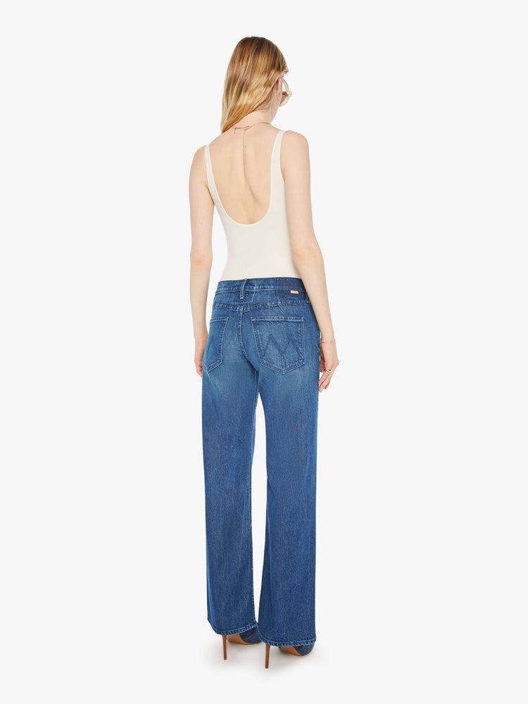Back view of a woman in a med blue high-rise bootcut with a zip fly, looser leg and a long 31-inch inseam with a clean hem.
