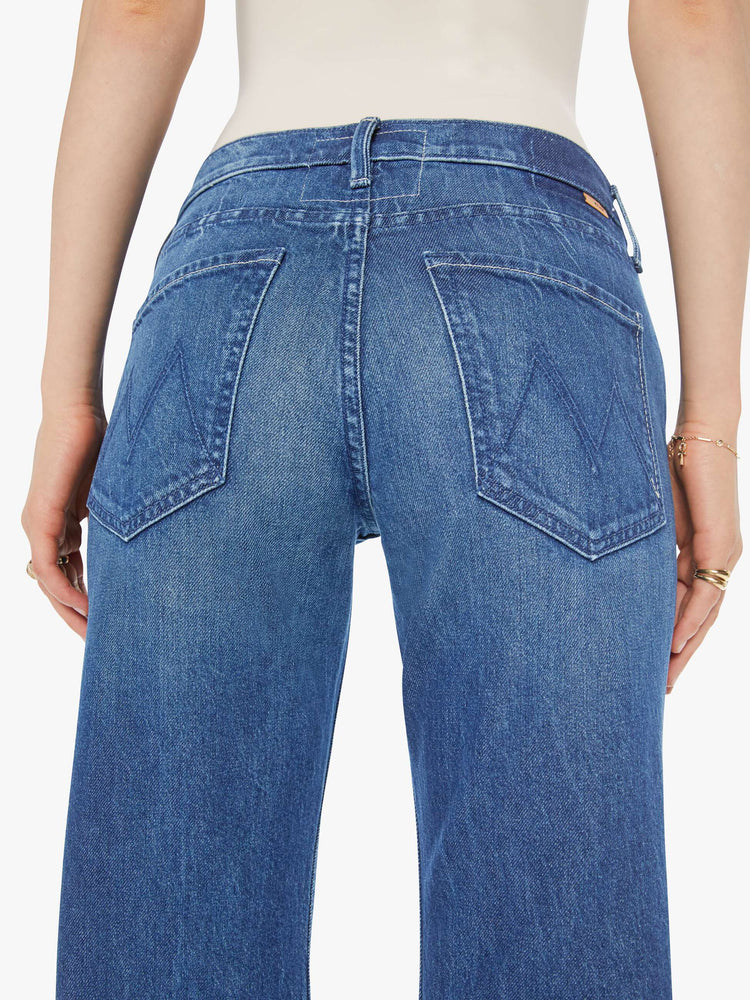Back close up view of a woman in a med blue high-rise bootcut with a zip fly, looser leg and a long 31-inch inseam with a clean hem.