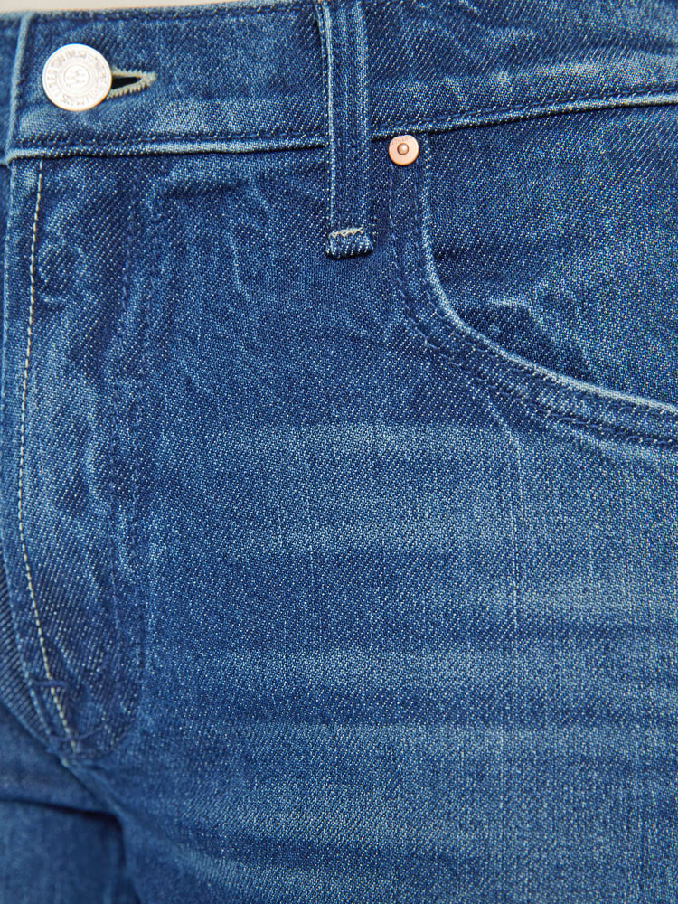 Swatch view of a woman in a med blue high-rise bootcut with a zip fly, looser leg and a long 31-inch inseam with a clean hem.