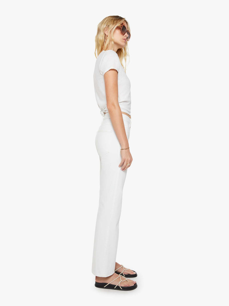 Side view of a woman in a white mid-rise bootcut with a zip fly, looser leg and a long 31-inch inseam with a clean hem.