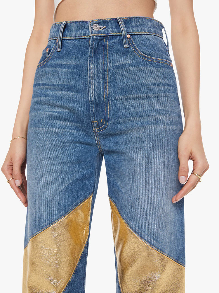 Close up view of a woman in a super high-waisted bootcut jeans with a zip fly and a long 34-inch inseam with a clean hem in a mid blue with gold spiral patches.