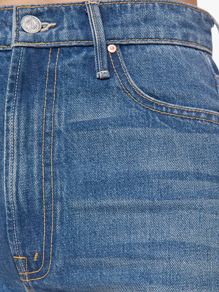 Swach view of a woman in a super high-waisted bootcut jeans with a zip fly and a long 34-inch inseam with a clean hem in a mid blue with gold spiral patches.
