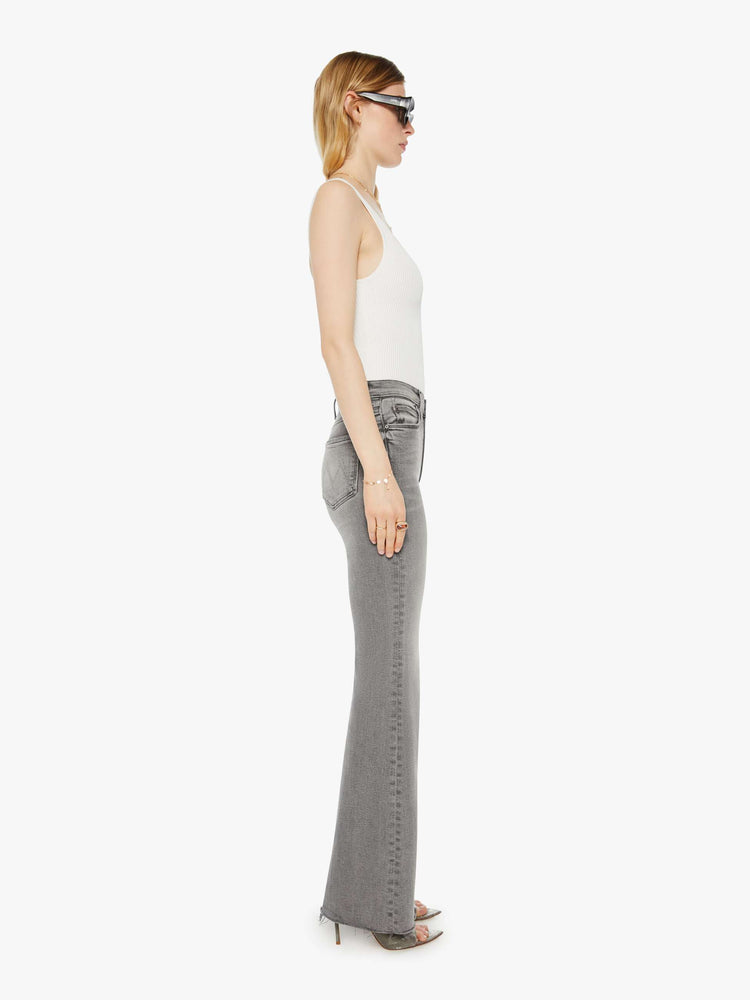 Side view of a woman in a light grey high rise flare  with a long 32-inch inseam, zip fly and a frayed hem.
