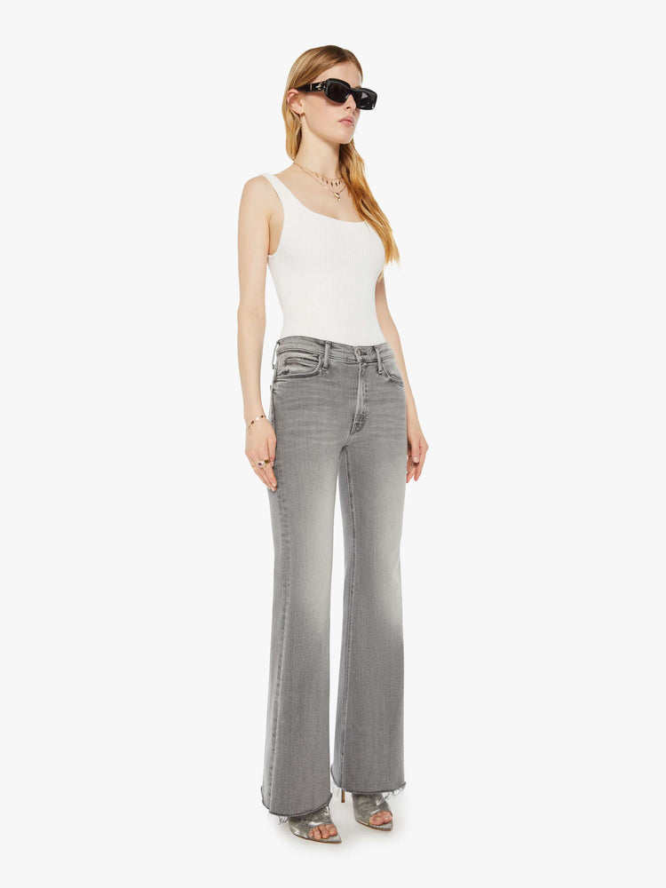 Side angle view of a woman in a light grey high rise flare  with a long 32-inch inseam, zip fly and a frayed hem. 